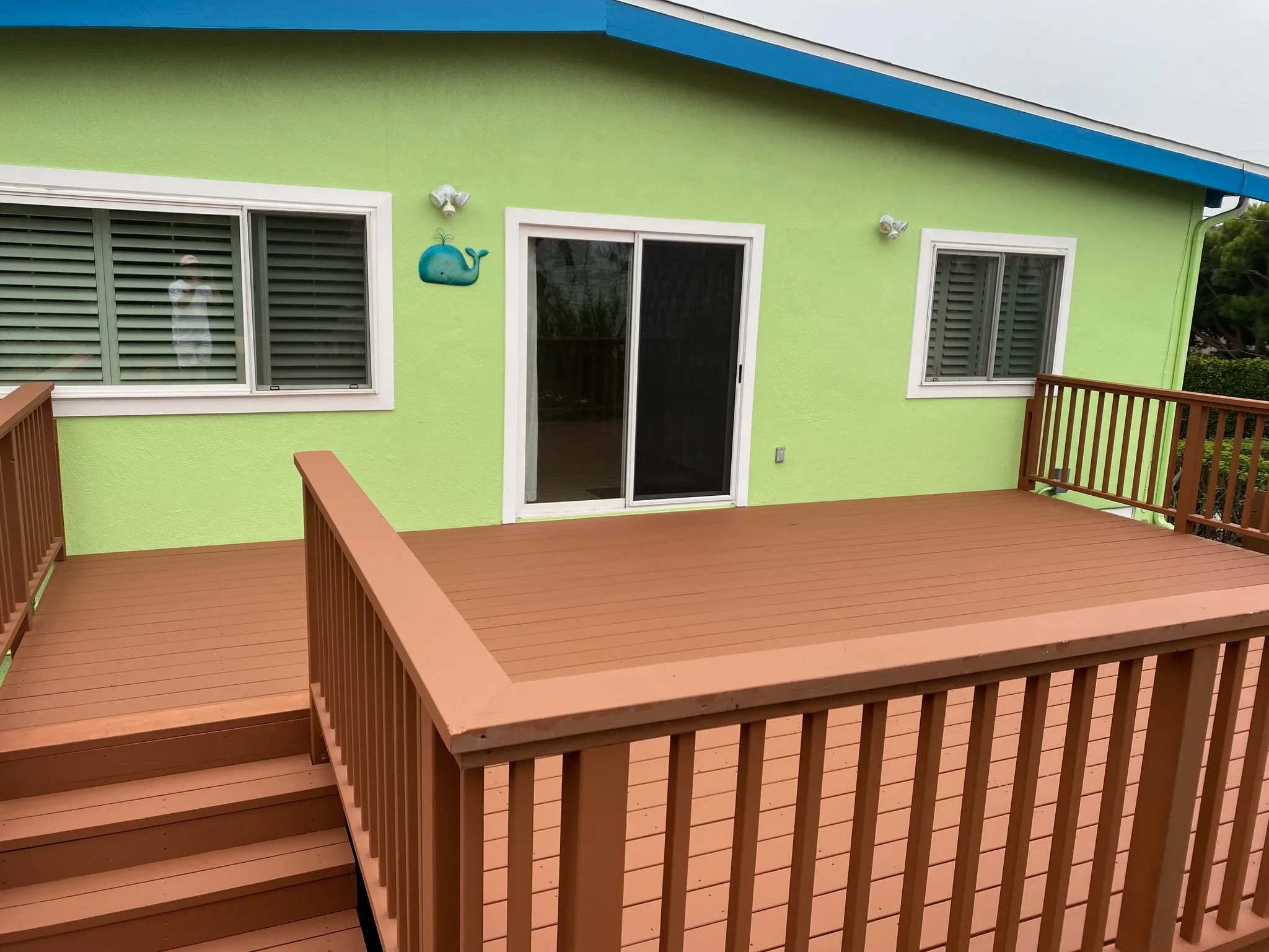 Redwood-toned refinished deck beside a green home
